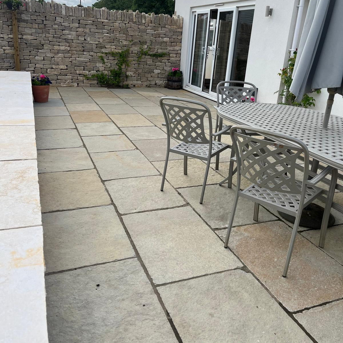 Outdoor patio area with stone pavement, chairs, and a table near a house.