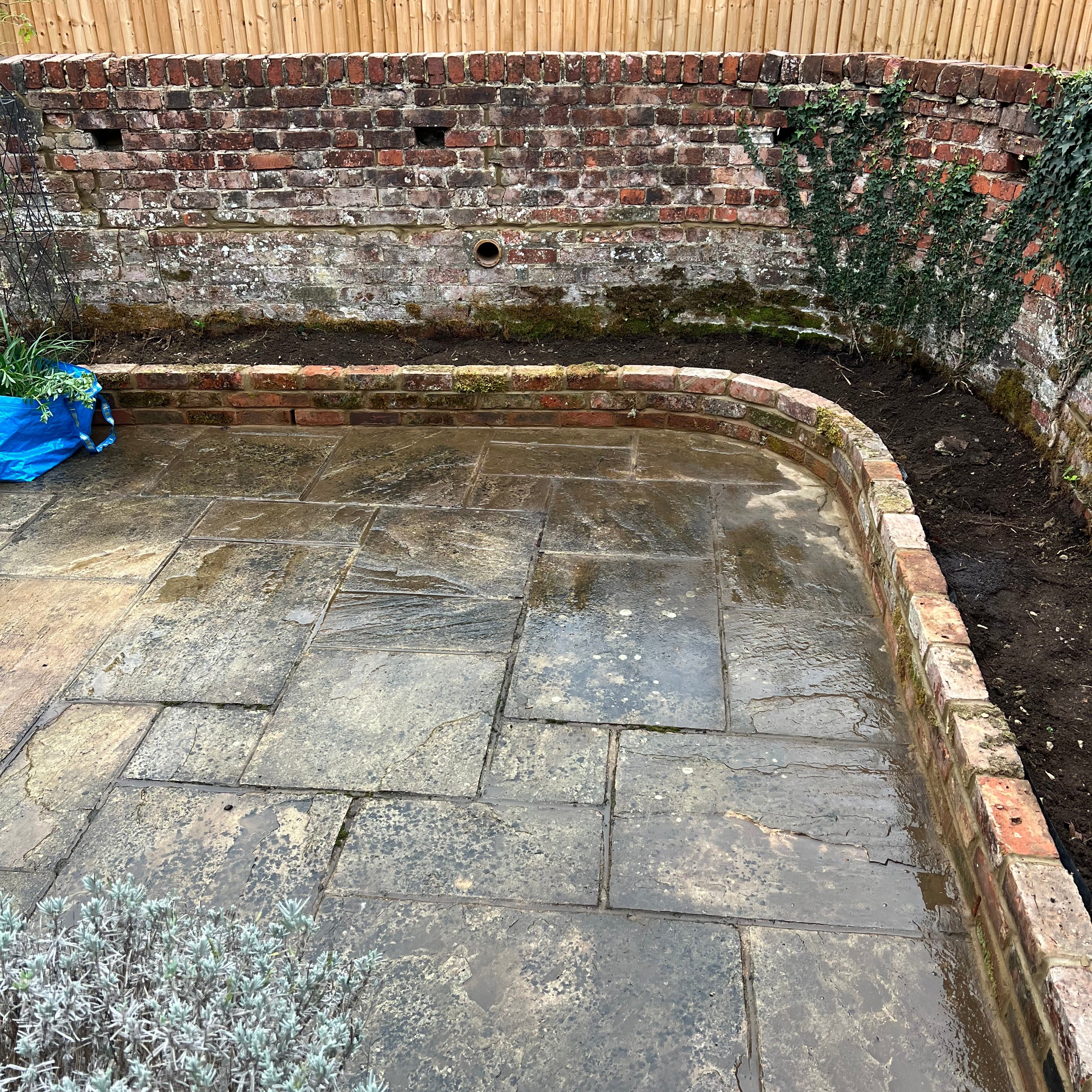 A low redbrick, retaining wall with soil inside to be used as a planter bed.