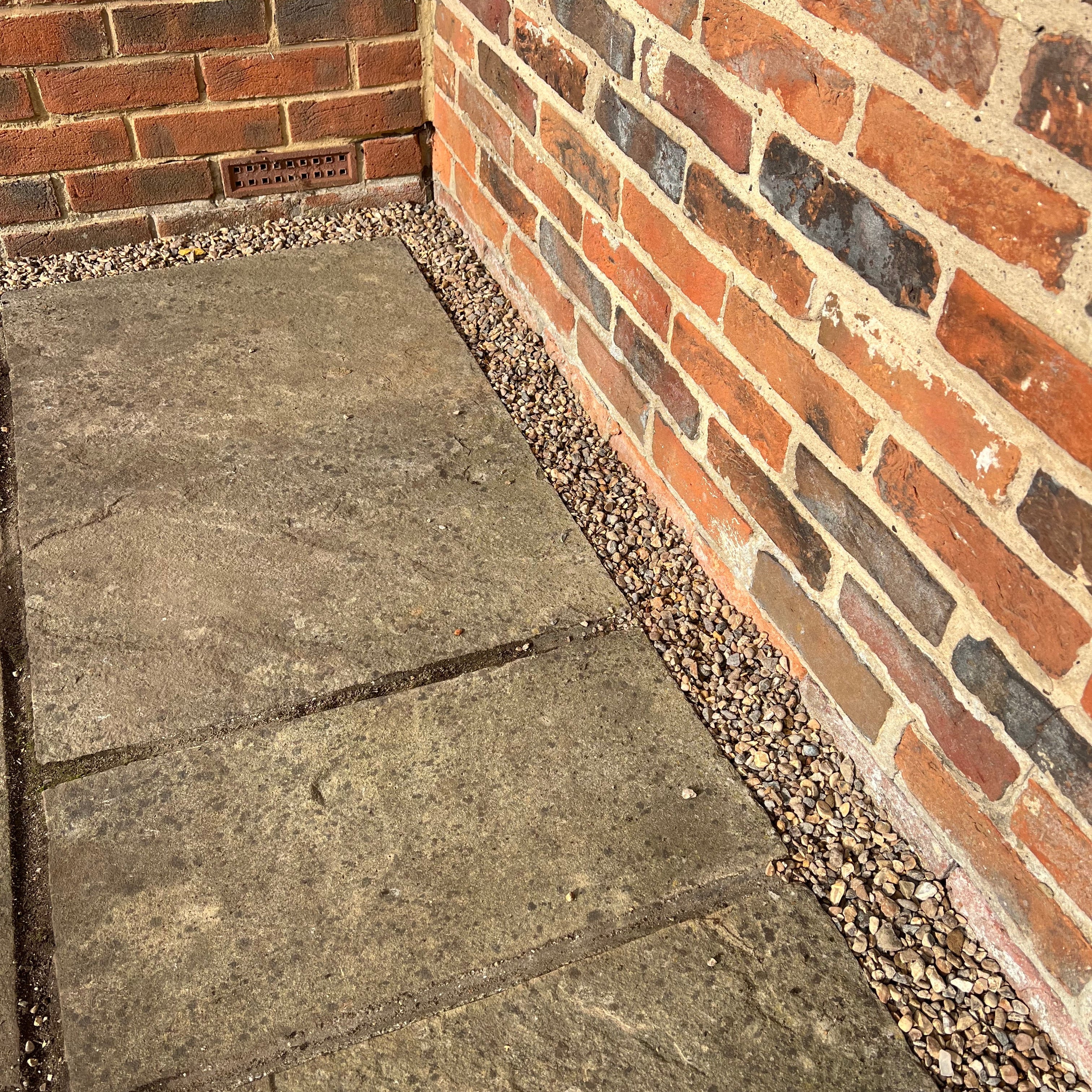 Soak away built next to Indian sandstone patio against redbrick house.