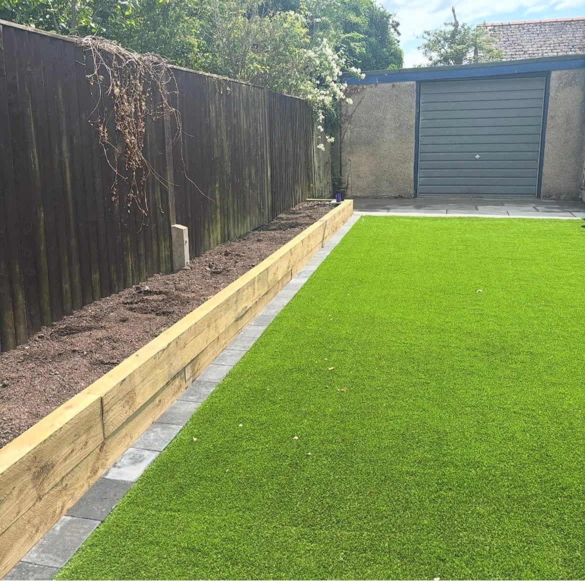 Garden with artificial grass, wooden sleeper bed, block paving boarder.
