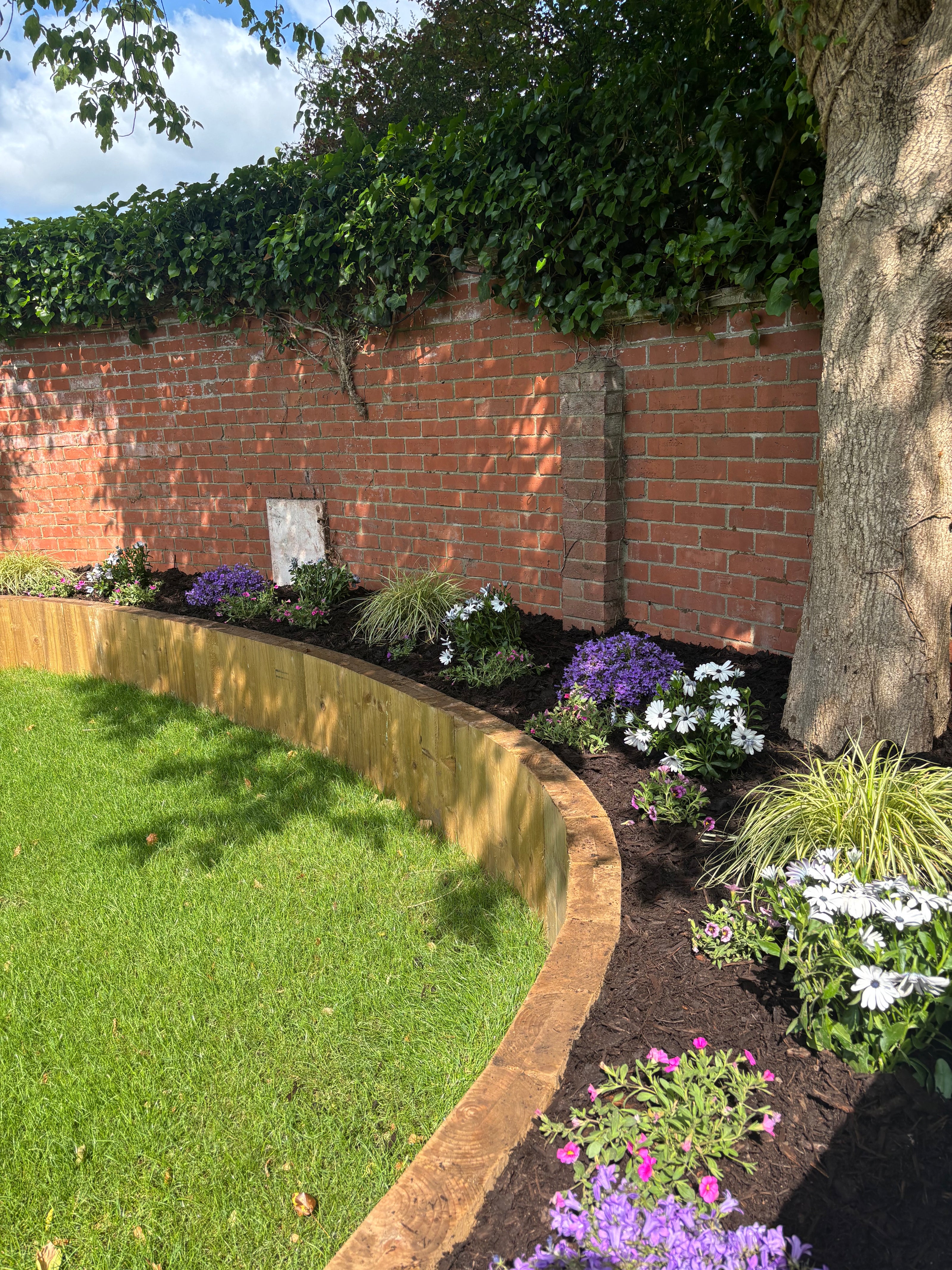 Garden with flowers, brick wall, sleeper retaining wall and grass.
